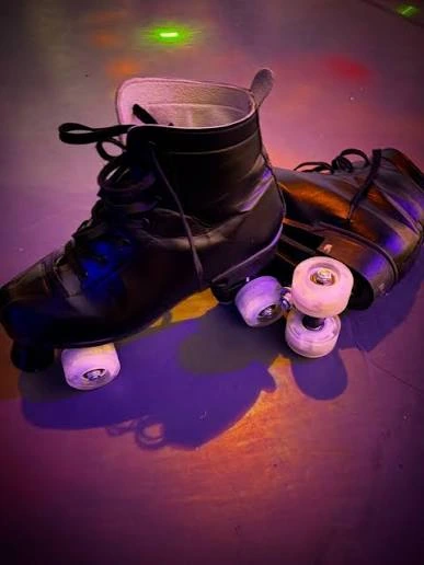 Black quad roller skates on a floor washed with purple and amber light
